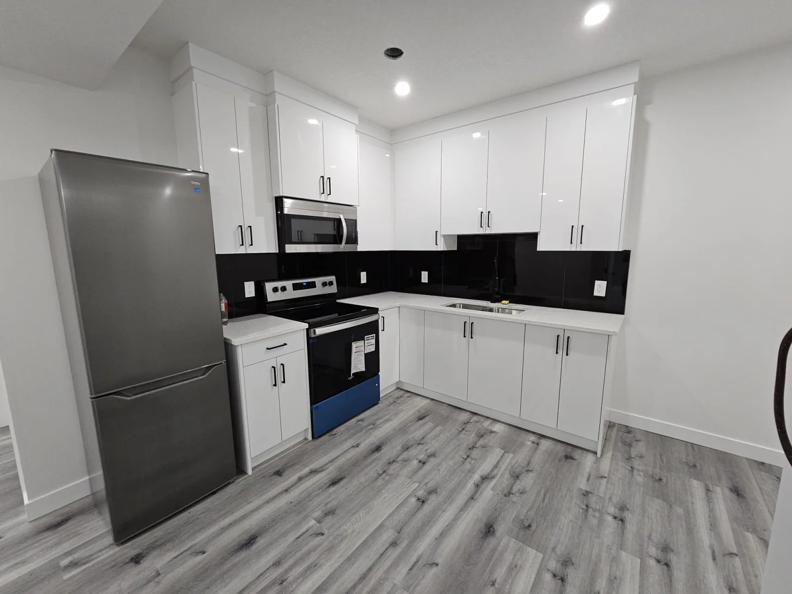 White kitchen with black countertop and backsplash and stainless appliances — Calgary basement suite
