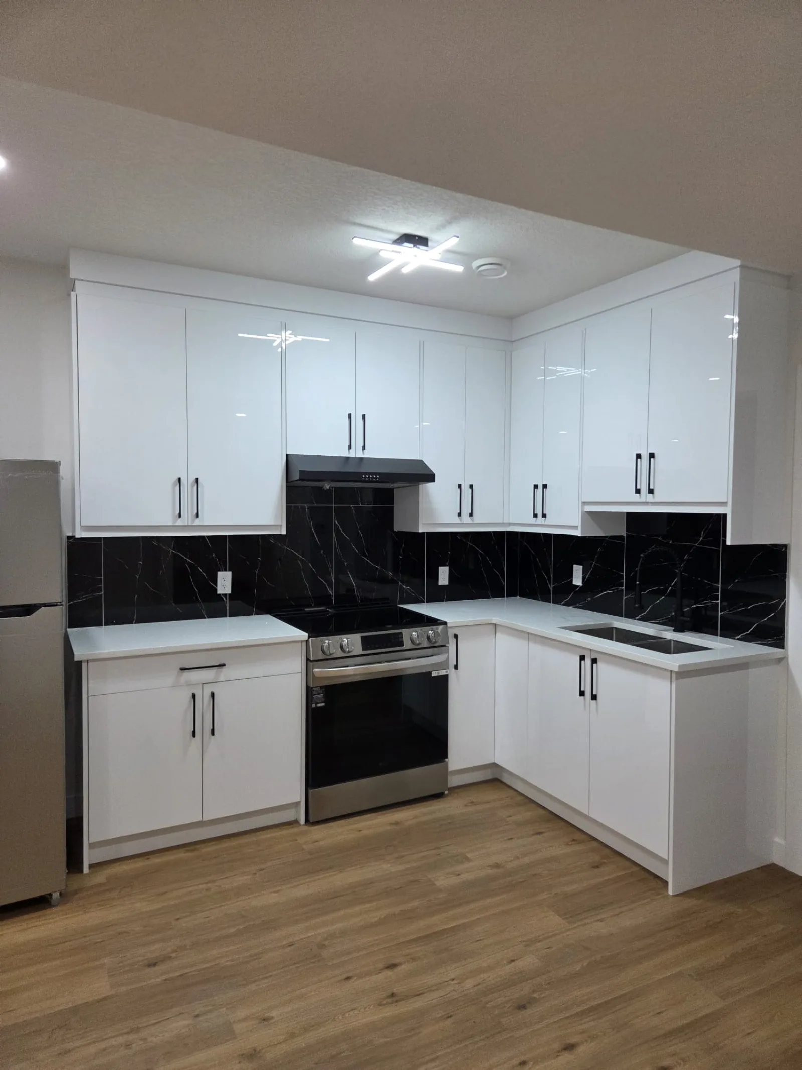White kitchen with black countertops, stainless appliances and wood-look flooring — Calgary