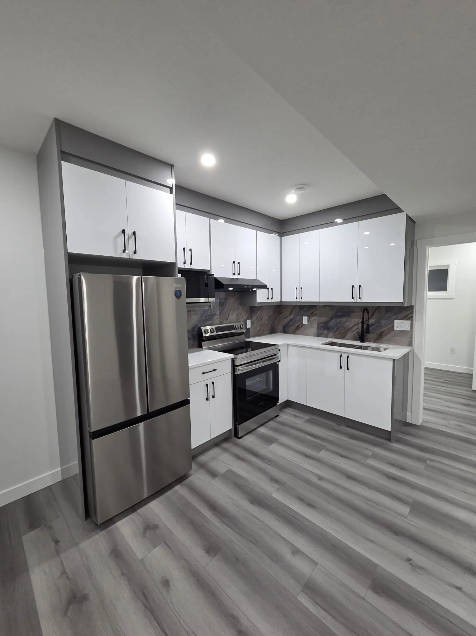 Open white kitchen with stainless appliances and grey vinyl plank flooring — Calgary secondary suite