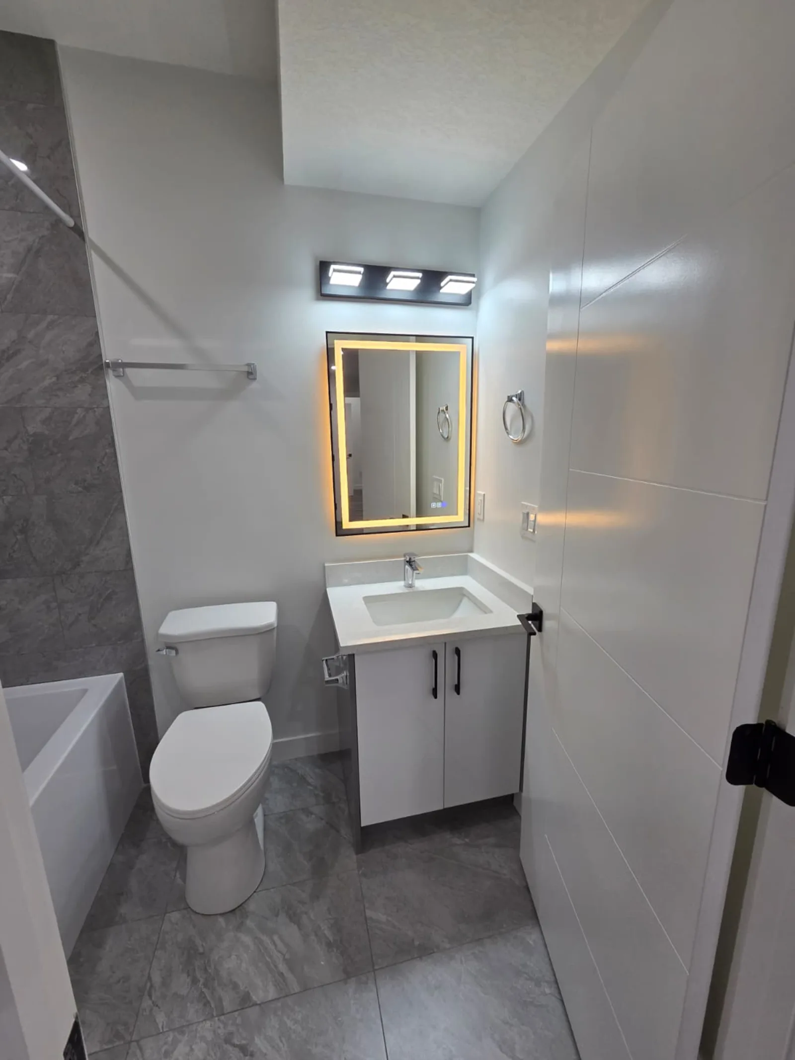 Bathroom with backlit mirror, vanity and grey tile flooring — Calgary suite